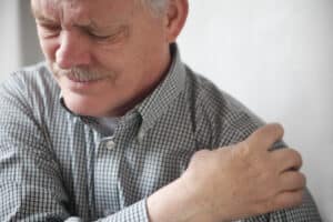 Senior gentleman grimacing from shoulder pain, showing stiffness and spasticity related to mobility or rehabilitation issues